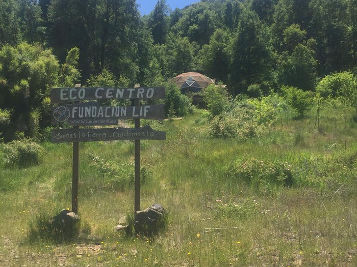 Letrero del Ecocentro Fundación LIF entre vegetación, con un domo al fondo